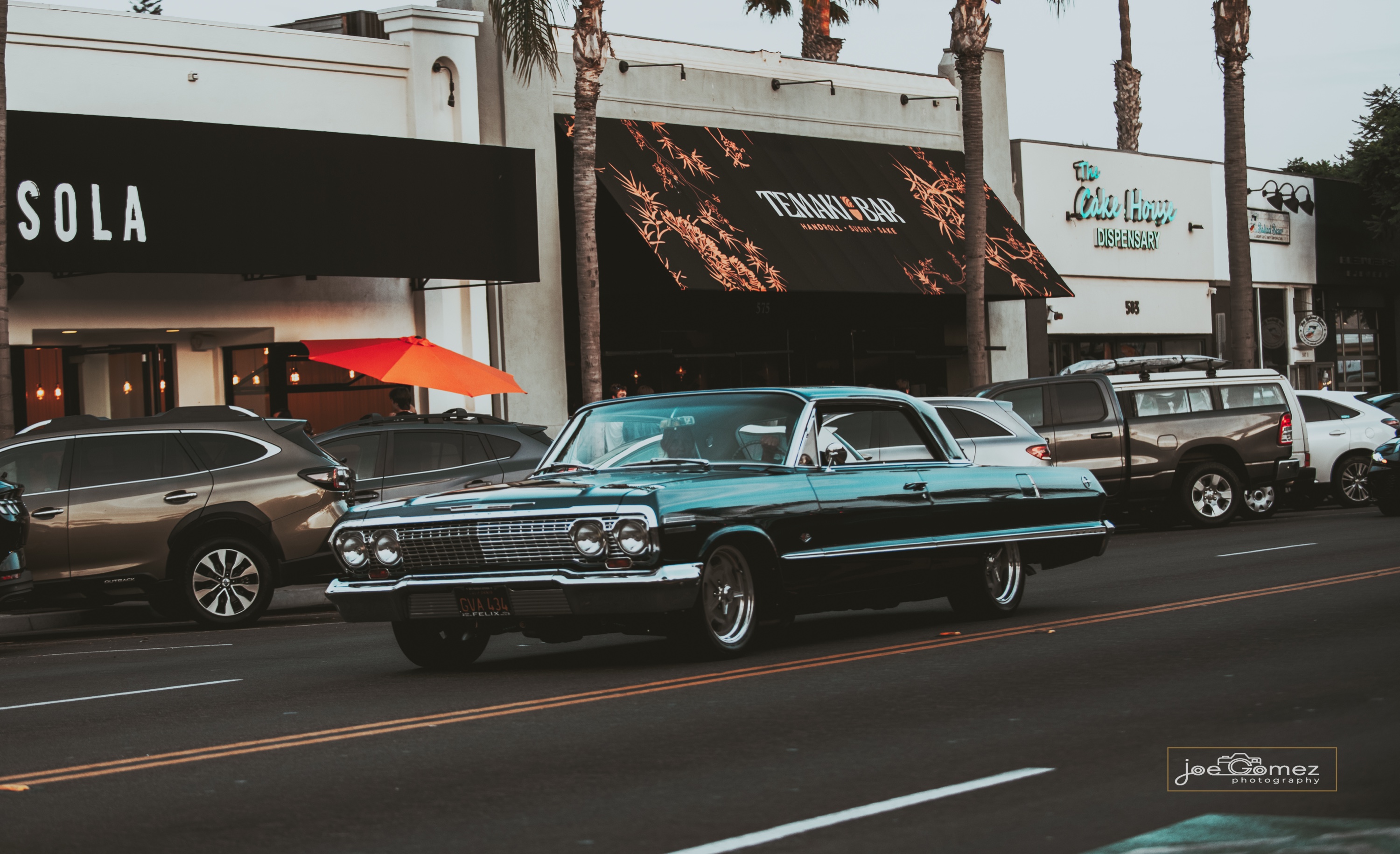Teal classic lowrider cruising past storefronts on Highway 101