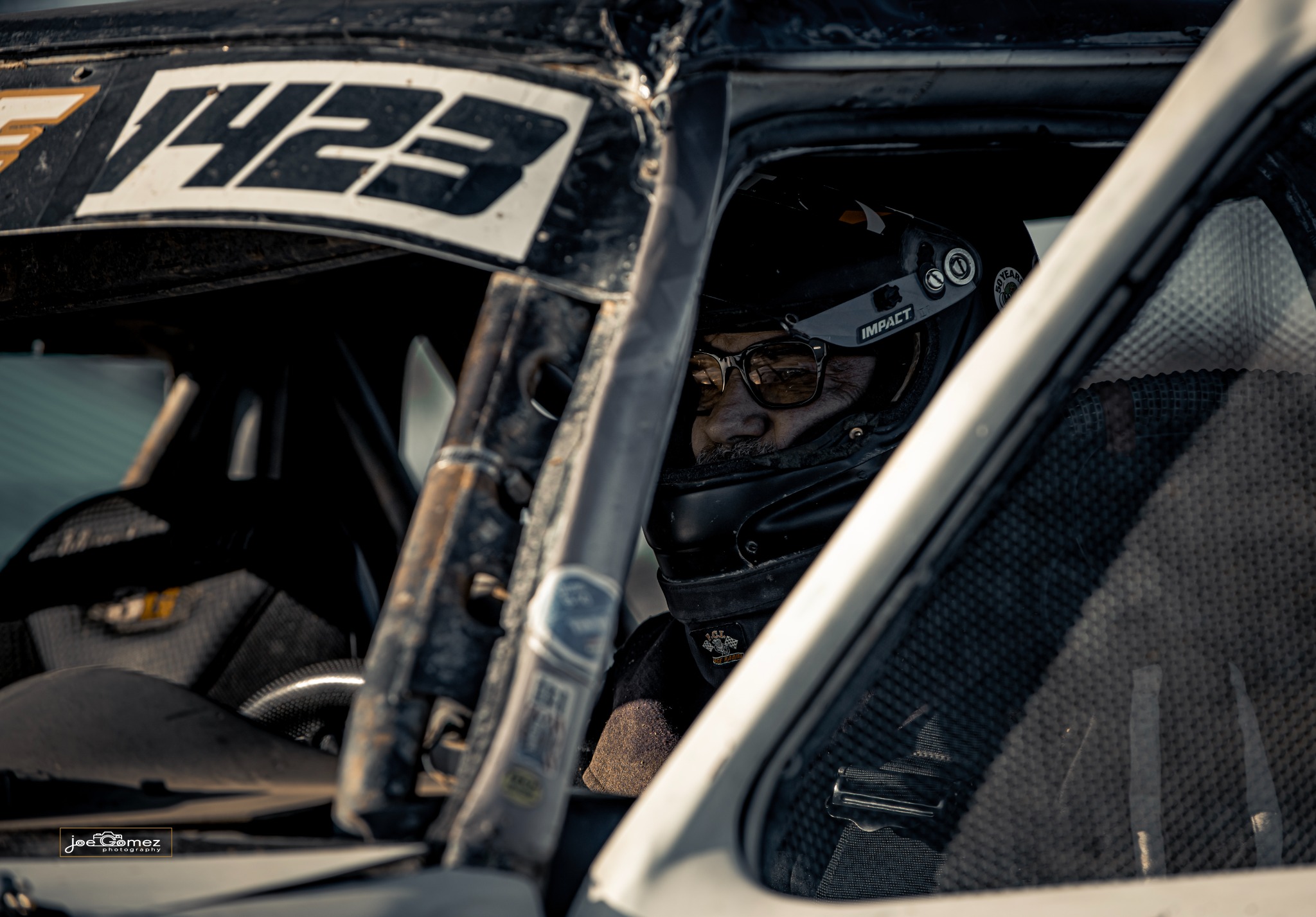 A helmeted driver wearing glasses seen through the vehicle’s cage tubing