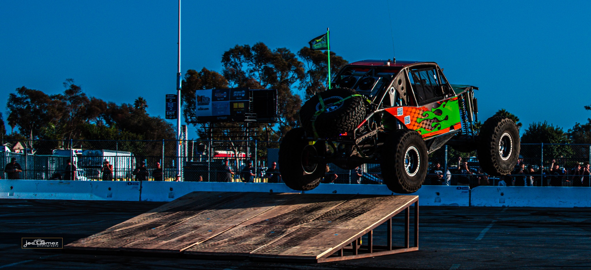 An orange and green off-road buggy airborne beside an arena ramp