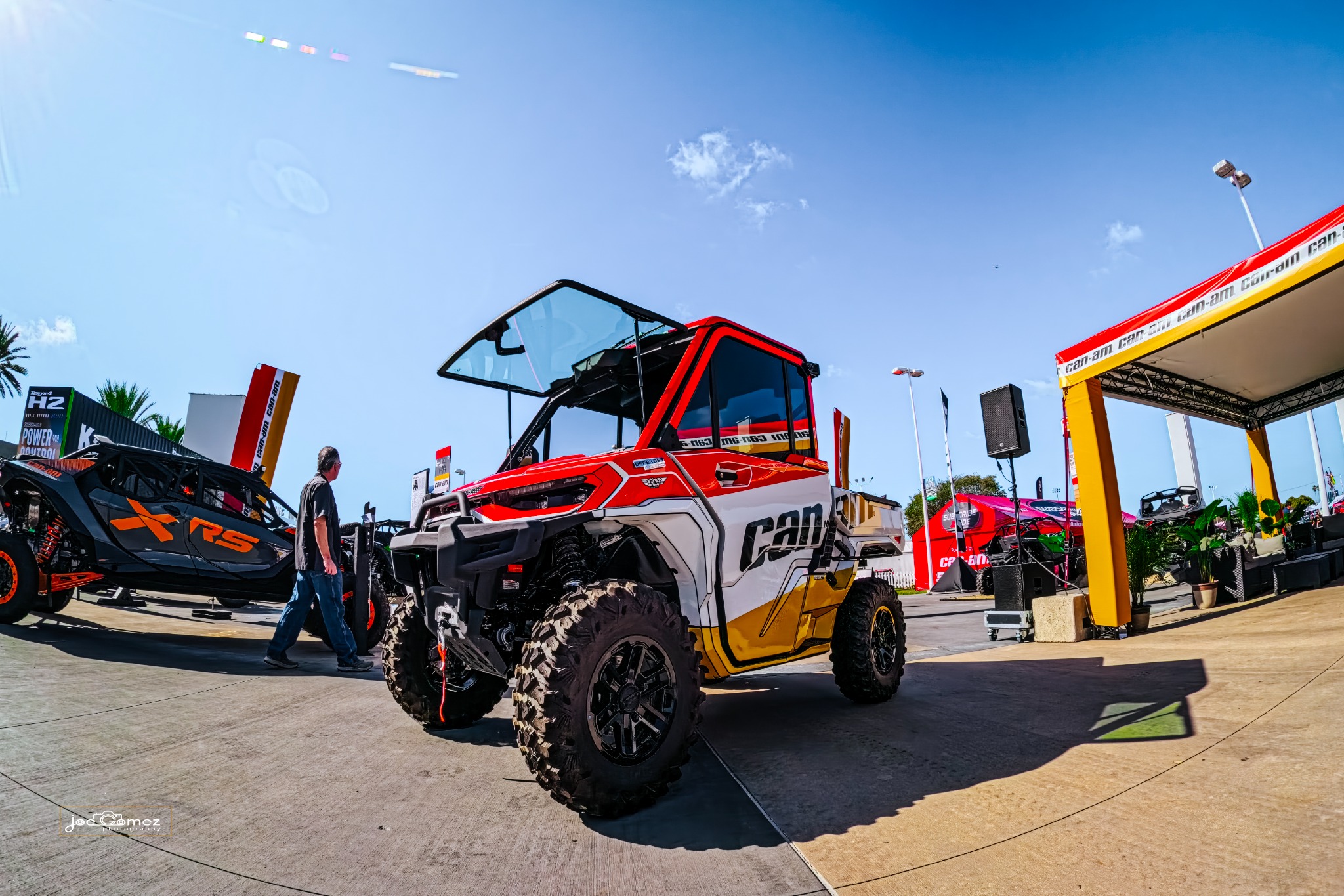 A red, white and yellow Can-Am utility vehicle with its windshield raised at an outdoor display
