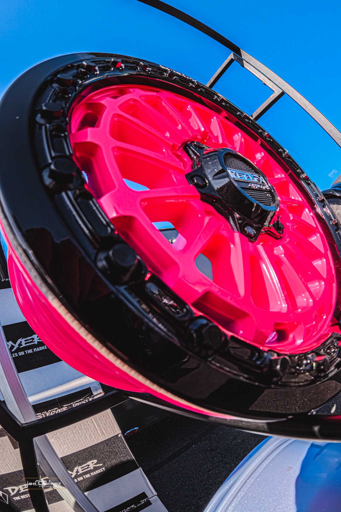 Close-up of a fluorescent pink display wheel with a black outer rim against a blue sky