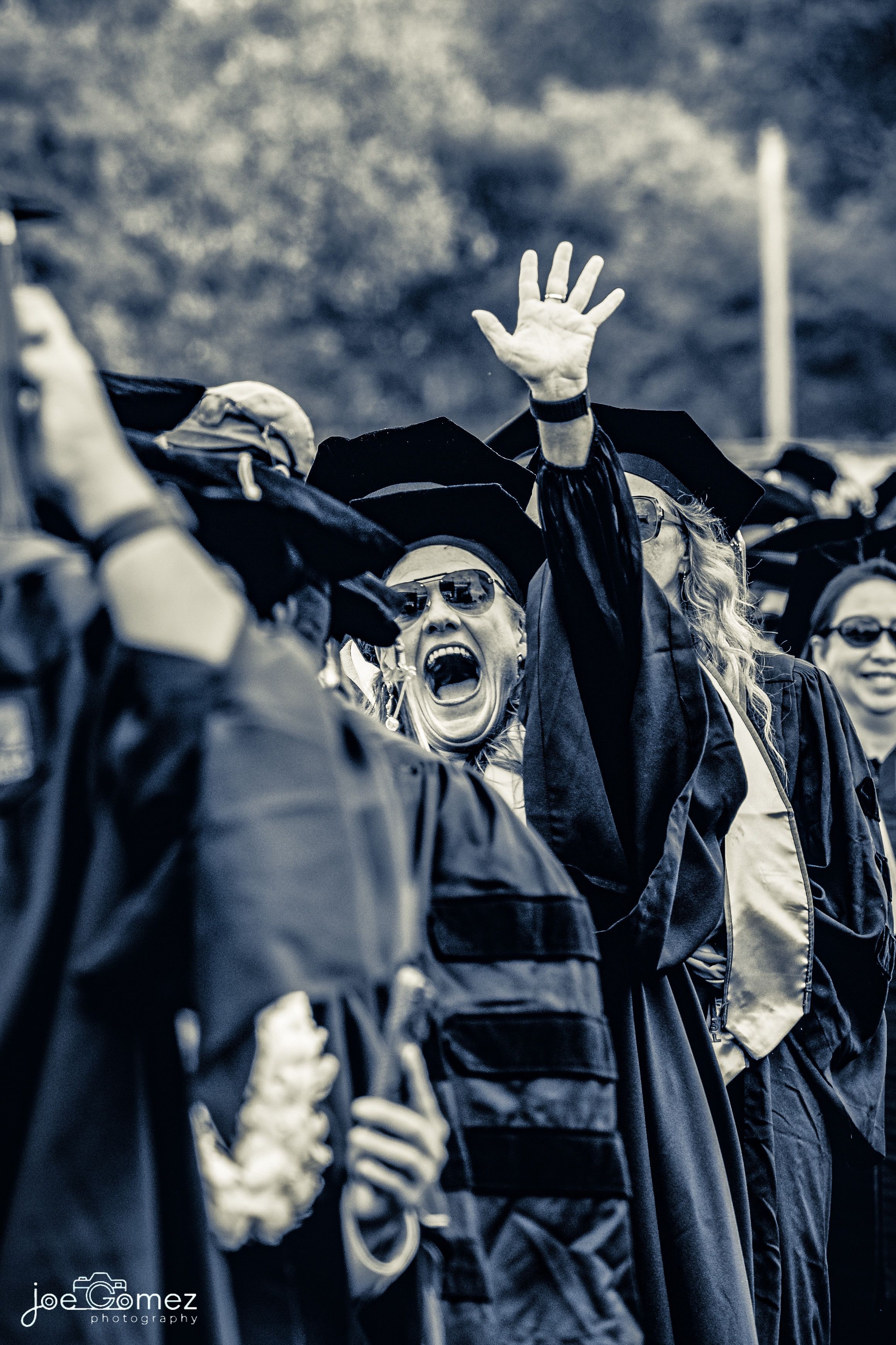 Black-and-white candid portrait of doctorate graduates cheering at commencement, photographed in Irvine, California by Joe Gomez.