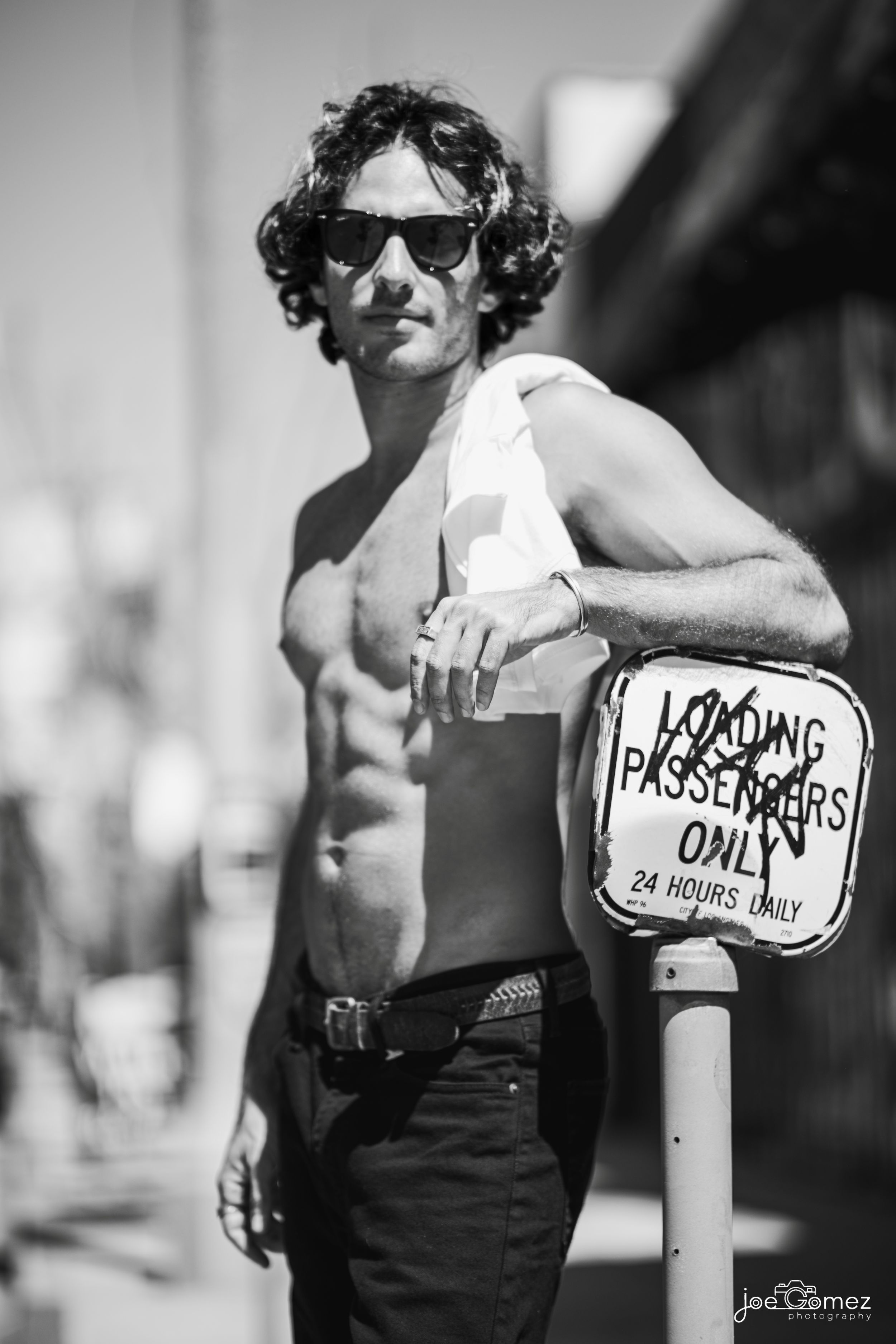 Black-and-white editorial portrait of a shirtless male actor leaning against a street sign in Southern California, photographed by Joe Gomez.