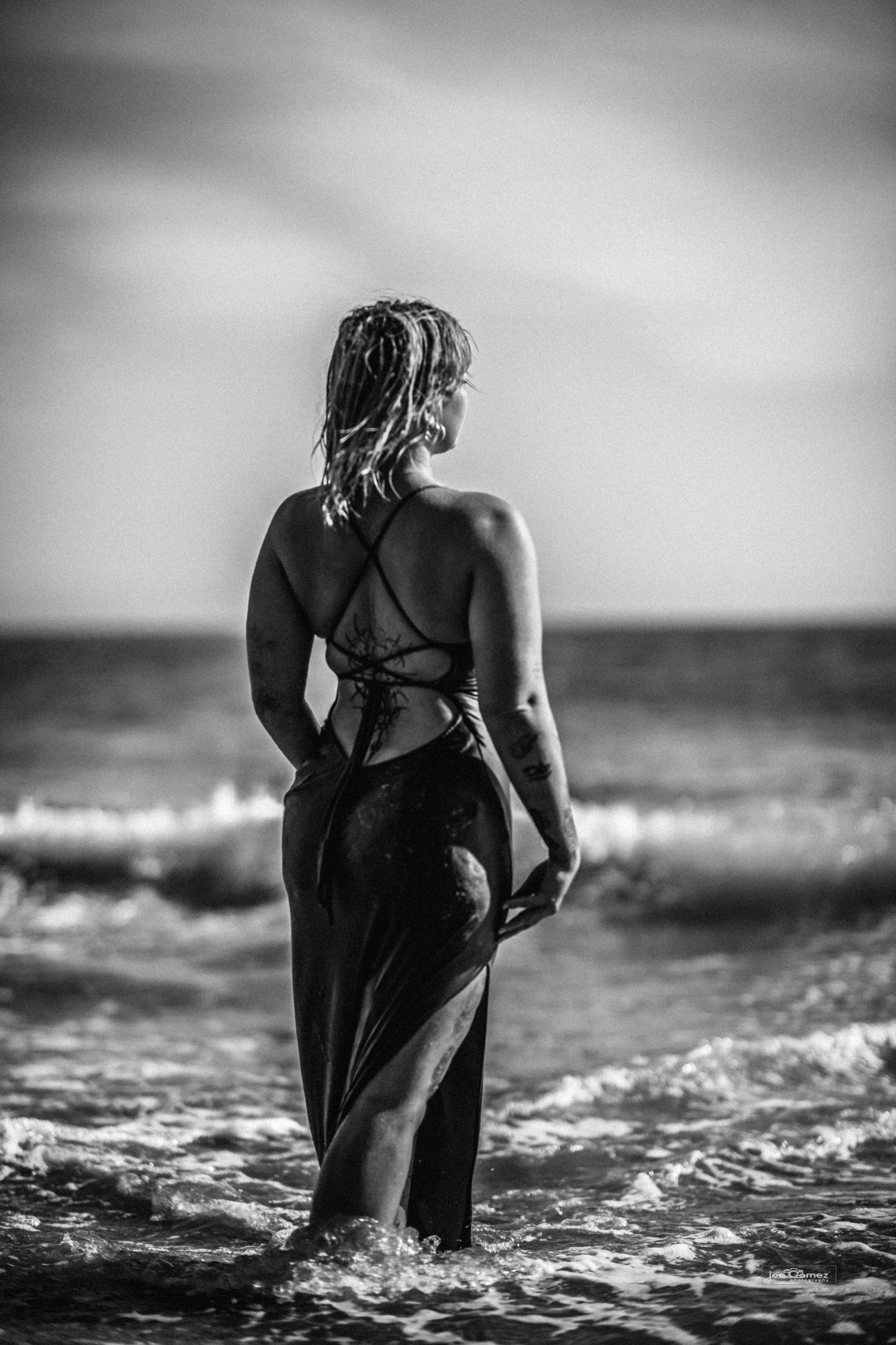 Black-and-white Malibu model photo shoot portrait of Mae standing in the Pacific surf at El Matador State Beach in Malibu, California, photographed by Joe Gomez.