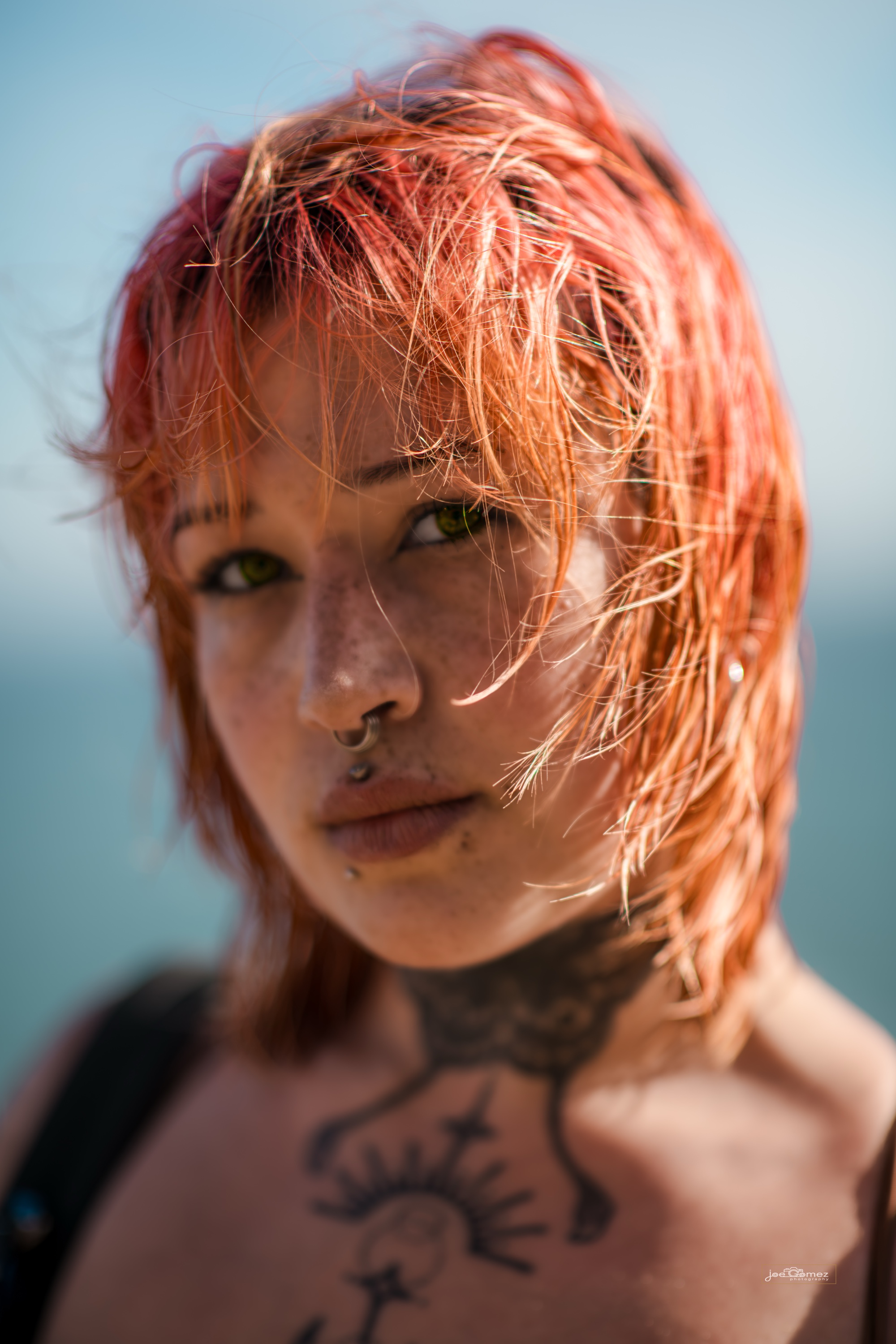 Close editorial beauty portrait of Mae with vivid red hair and direct eye contact at El Matador State Beach in Malibu, California, photographed by Joe Gomez.