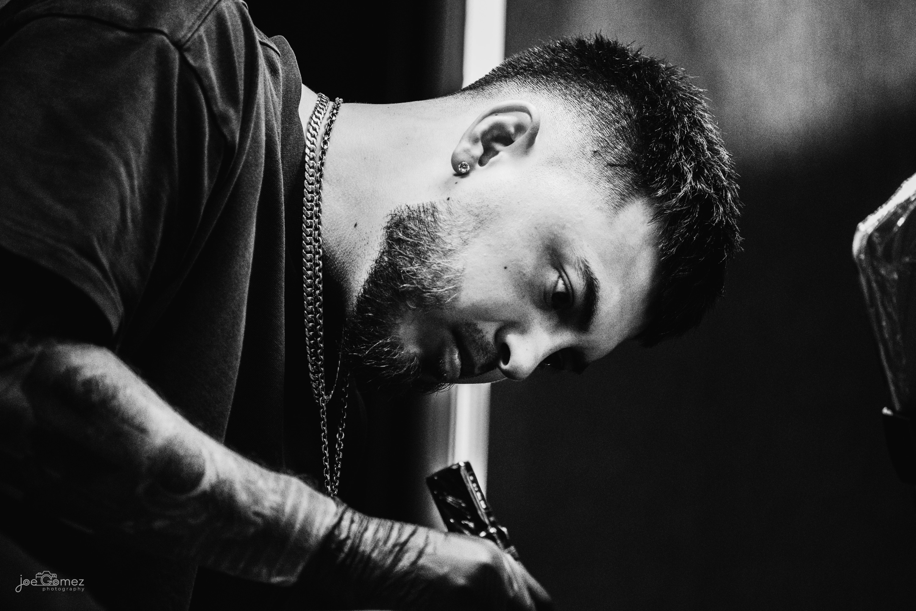 High-contrast black-and-white documentary portrait of a tattoo artist concentrating on his craft in a Southern California tattoo studio, photographed by Joe Gomez.