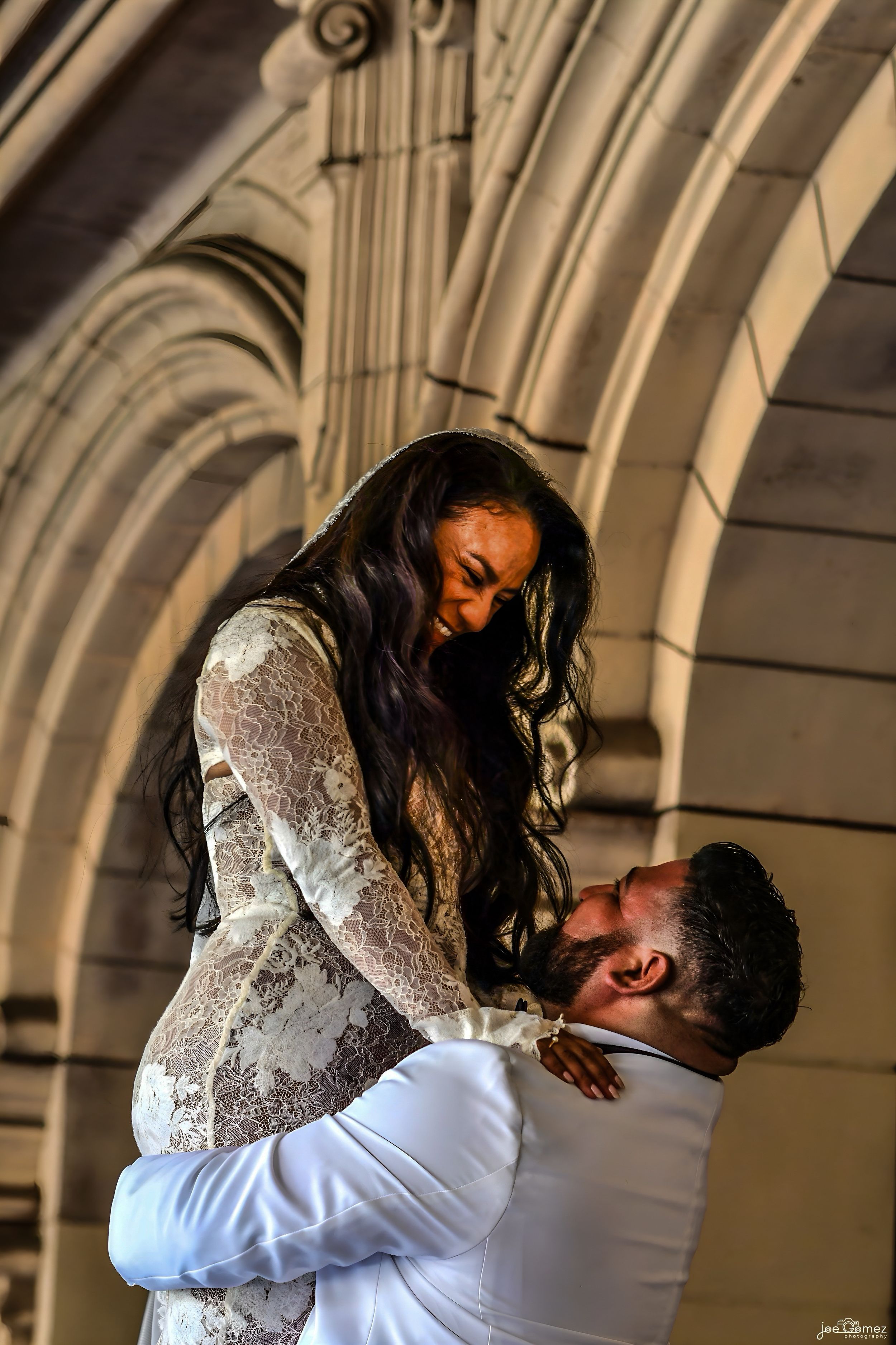 Joyful wedding portrait of a groom lifting and kissing his bride beneath the arches of Balboa Park in San Diego.
