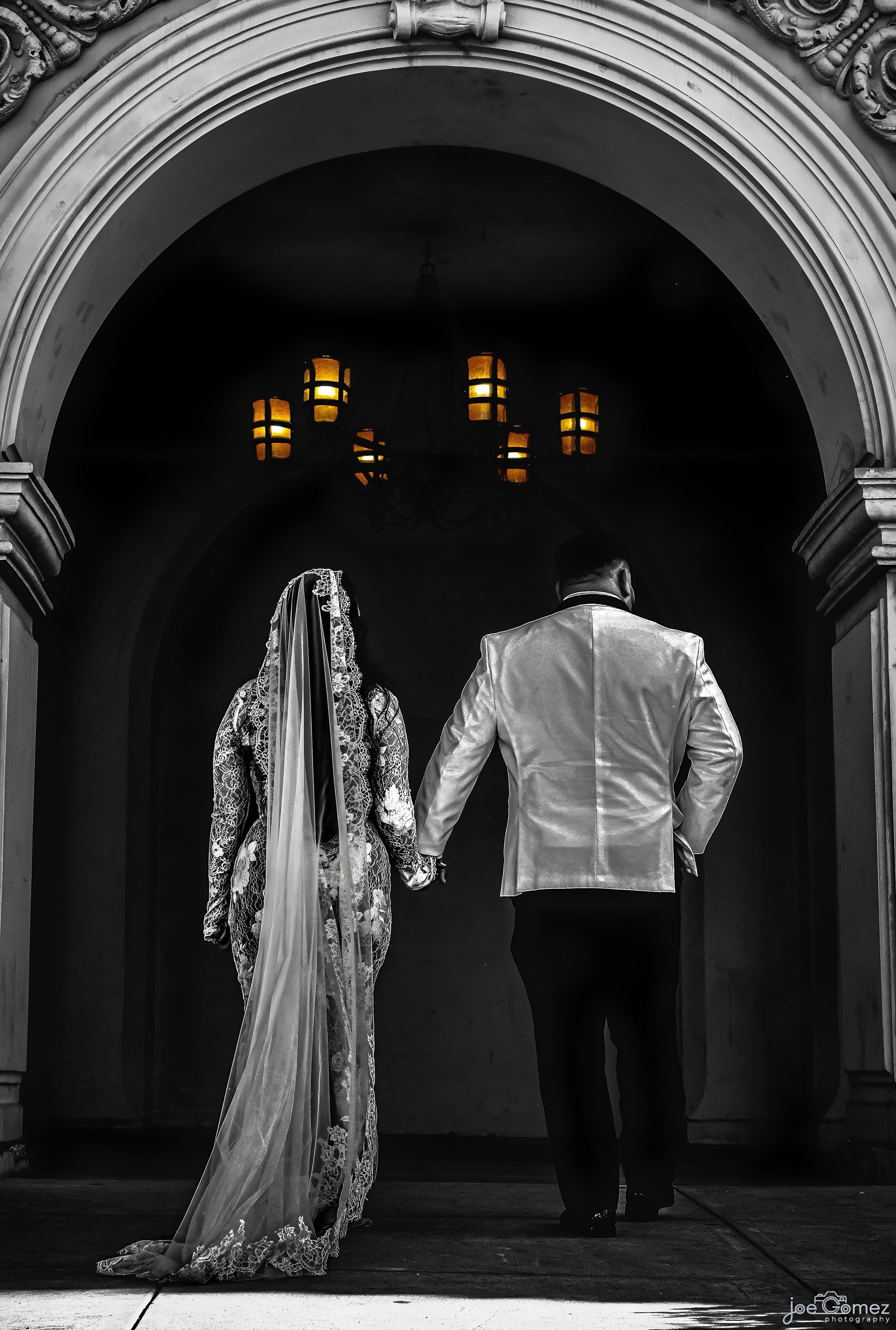 Black-and-white architectural wedding portrait of a bride and groom framed beneath a grand San Diego archway.