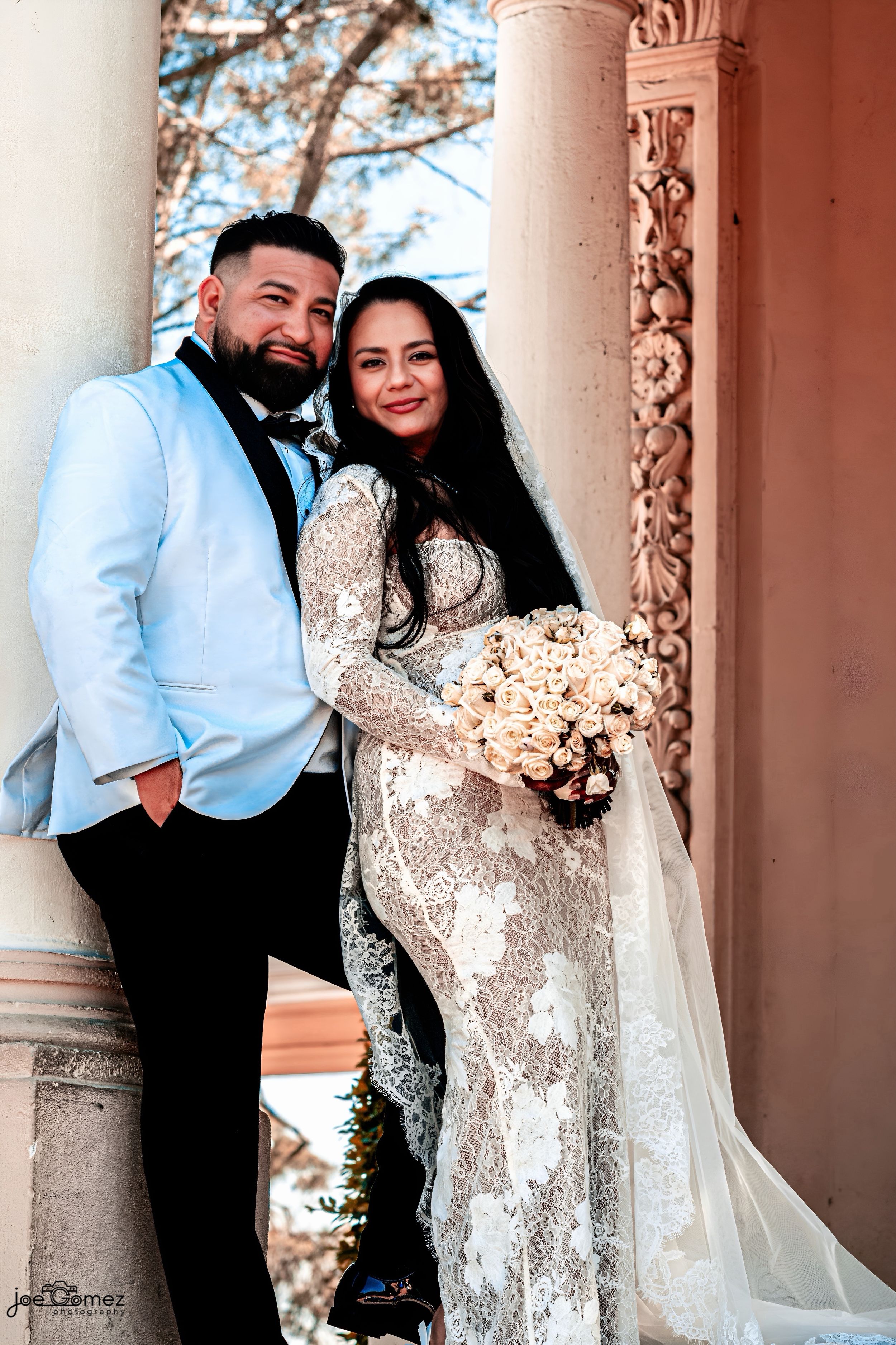 Warm natural-light wedding portrait of newlyweds embracing beside historic Balboa Park architecture.
